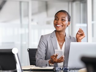 Business Professional Smiling at Desk with Smartphone and Laptop