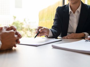 Close-up of two professionals in a business meeting, with one person holding a pen and pointing at a document on a clipboard